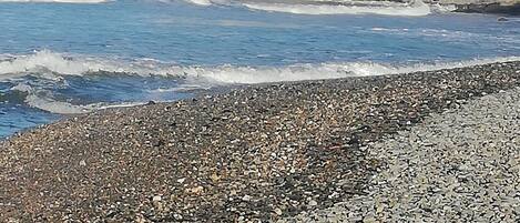 A pebble beach with waves, cliffs, and sparse vegetation.
