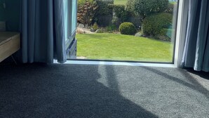Una habitación con un gran ventanal corredero que da a un balcón con vistas al mar y un jardín bien cuidado.