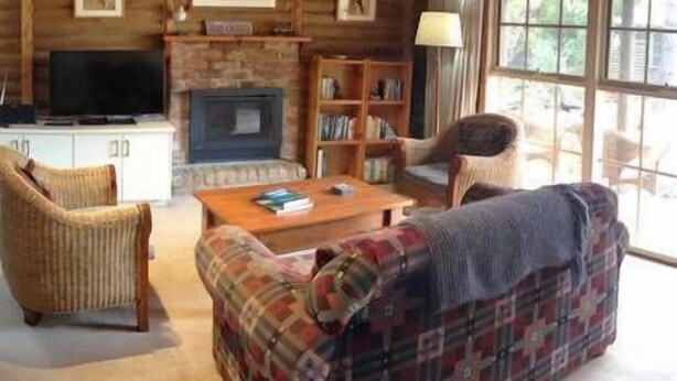 Accogliente interno di una baita in legno con camino, televisione, libreria e divano a quadri.