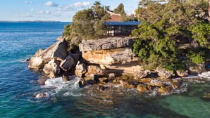 A coastal property with a house on a rocky outcrop, clear blue sea, and lush greenery.
