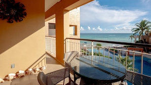 En balkon med et glasbord og stole, der giver udsigt over en pool og havet.