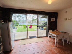 A kitchen with a refrigerator, a dining table with chairs, and a sliding glass door leading to a patio with chairs and a view of a garden.