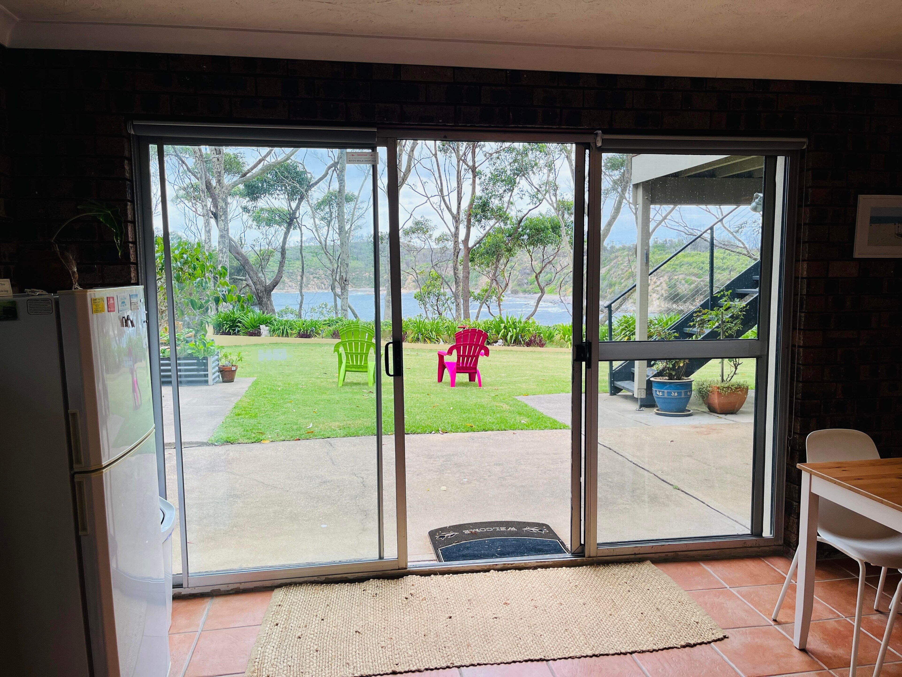 A room with a sliding glass door leading to a patio with a view of the ocean, a refrigerator, and a dining area with a table and chairs.
