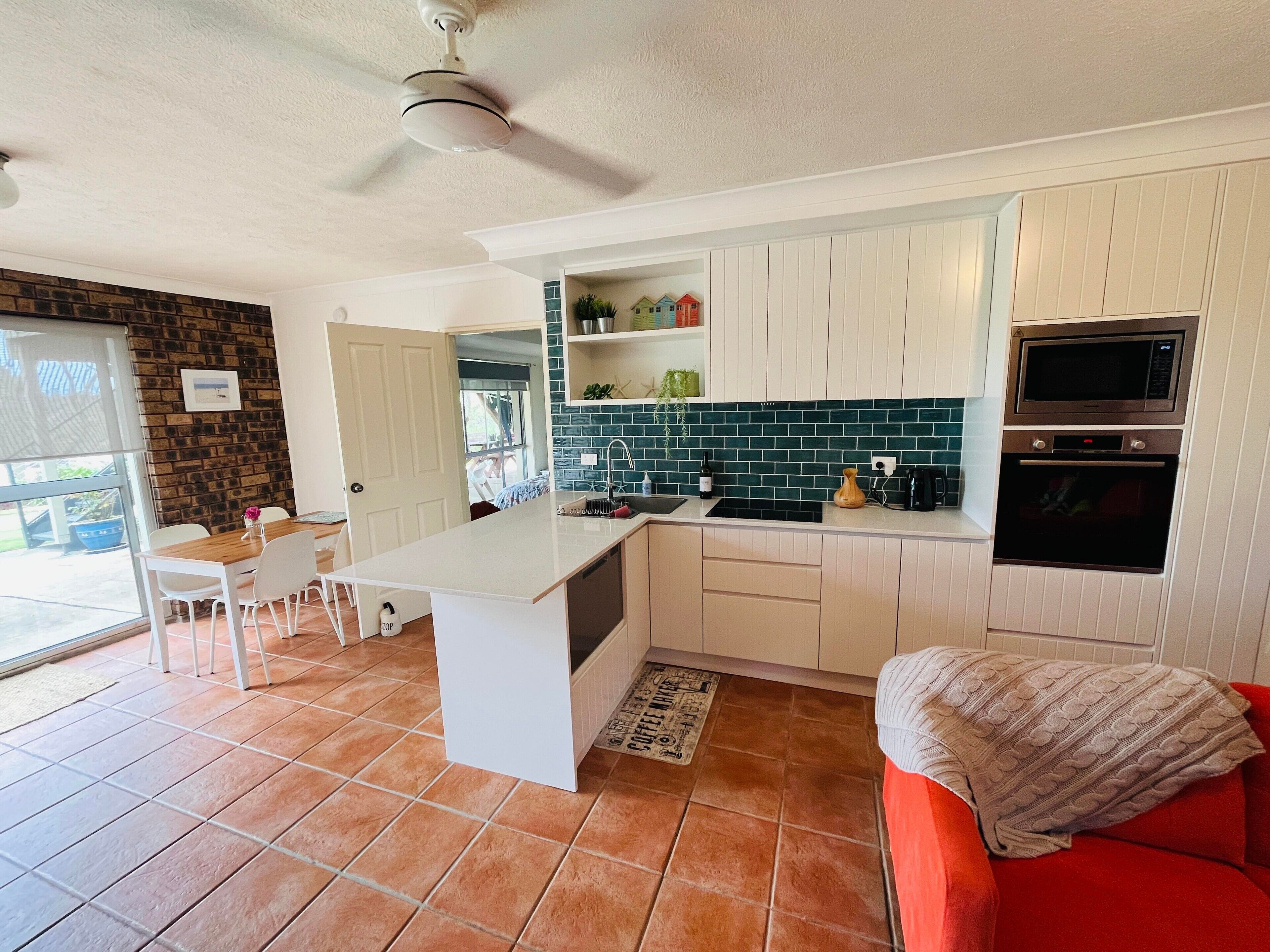 A compact kitchen with white cabinets, a built-in microwave, and an oven. There's a dining area with a table and chairs, and a red sofa in the living space.