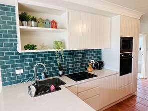 Une cuisine moderne avec des meubles blancs, un évier noir et un pare-feu turquoise.