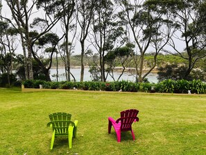 Deux chaises sur une pelouse verdoyante, avec vue sur une étendue d’eau et des arbres en arrière-plan.