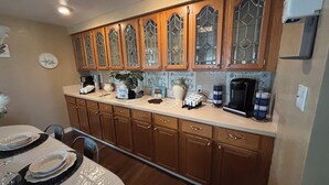 Una cocina con armarios de madera, una estación de café y un comedor con una mesa preparada para dos.