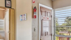 Una habitación con puerta de madera, un extintor, un cartel que dice 'Beach' y una ventana con vista a un parque infantil.