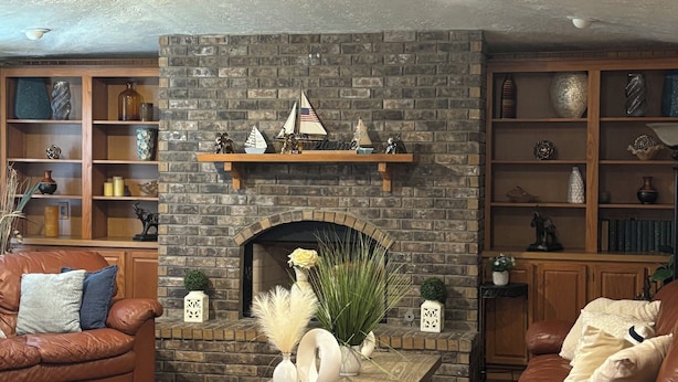 Una sala de estar con chimenea de piedra, sofás de cuero, estanterías de madera y un ventilador de techo.