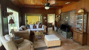 A spacious living room with a high ceiling, a sofa set, a television, and a cabinet with glass doors. - Sebring Lakefront Home - Lake Josephine 'Little Piece Of Heaven' (Sebring)