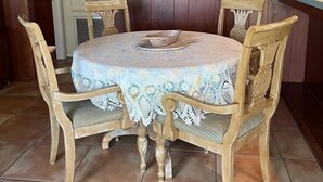 A dining area with a round table covered by a lace tablecloth, surrounded by four wooden chairs with cushioned seats. Above the table hangs a stained glass pendant light and a framed painting of sunflowers. - Sebring Lakefront Home - Lake Josephine 'Little Piece Of Heaven' (Sebring)