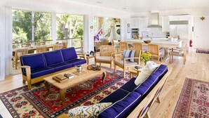 A spacious living room with a blue sofa, wooden chairs, a coffee table, and a large window offering a view of trees. - Private Island Retreat with Private Beach,  Dock, Palm Trees & Glorious Sunsets (Longboat Key)