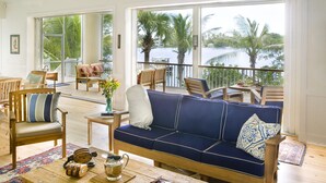 A spacious living area with a blue sofa, wooden chairs, and a view of a lake with palm trees. - Private Island Retreat with Private Beach,  Dock, Palm Trees & Glorious Sunsets (Longboat Key)