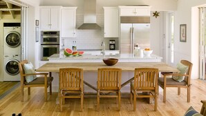 A modern kitchen with white cabinetry, a central island with chairs, a built-in oven, and a large refrigerator. - Private Island Retreat with Private Beach,  Dock, Palm Trees & Glorious Sunsets (Longboat Key)