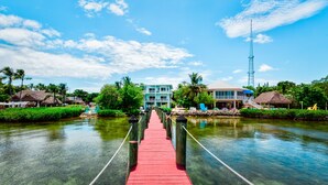 A wooden bridge leading to a resort with a pool and a building with a blue facade. - Key Largo Sunset Estate (Key Largo)