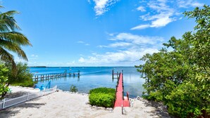 A beach with a wooden pier leading to the water, surrounded by greenery and a white fence. - Key Largo Sunset Estate (Key Largo)
