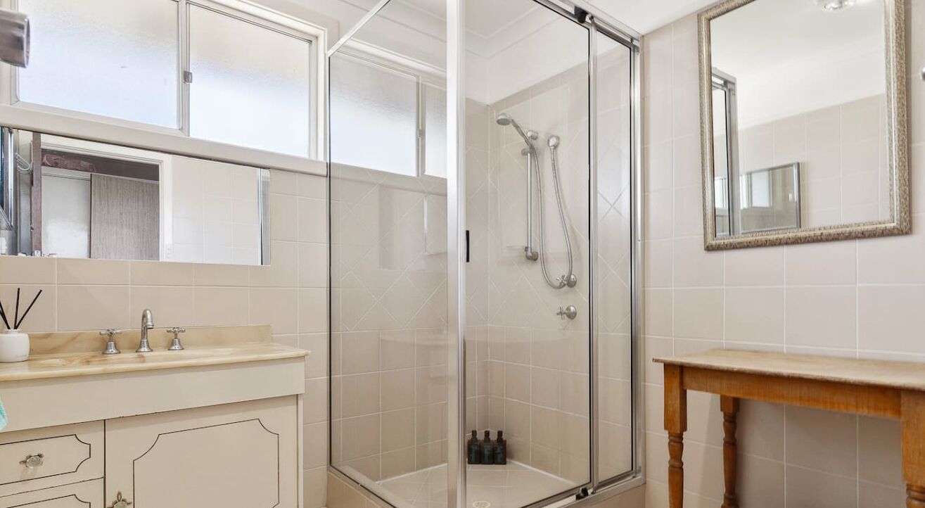 Une salle de bain avec une douche à parois de verre, un lavabo avec un miroir et un meuble-lavabo en bois.