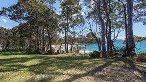 A coastal area with trees, a grassy foreground, and a beach in the background. - Windarra on Denhams Unit Three (Denhams Beach)