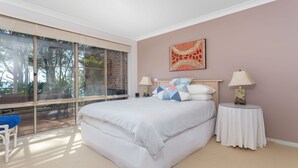 A bedroom with a large window, a bed with a quilt, two bedside tables with lamps, and a wall art piece. - Windarra on Denhams Unit Three (Denhams Beach)