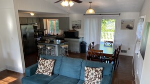 A modern living room with a blue sofa, a dining table, and a kitchen in the background. - Light & Open Family Beach House Short Walk to Kelly Beach (Narragansett)