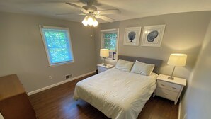A bedroom with a bed, two bedside tables with lamps, a ceiling fan, and two windows with blinds. - Light & Open Family Beach House Short Walk to Kelly Beach (Narragansett)
