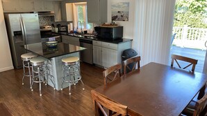 A modern kitchen with a central island, bar stools, and a dining table with chairs. - Light & Open Family Beach House Short Walk to Kelly Beach (Narragansett)