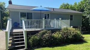 A house with a covered porch, a staircase leading to the deck, and a small garden area with bushes and flowers. - Light & Open Family Beach House Short Walk to Kelly Beach (Narragansett)