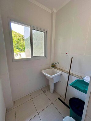 A small bathroom with a window, a sink, a trash bin, and a green shelf. - NEW APARTMENT, COND. HIGH STANDARD ON THE GRANDE BEACH INTEGRATED THE FOREST EXUBERENCE (UBATUBA)
