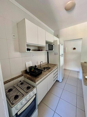 A kitchen with white cabinets, a gas stove, a microwave, and a refrigerator.