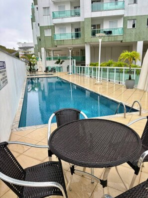 A swimming pool with a tiled deck, surrounded by a building with balconies and a signboard. - NEW APARTMENT, COND. HIGH STANDARD ON THE GRANDE BEACH INTEGRATED THE FOREST EXUBERENCE (UBATUBA)