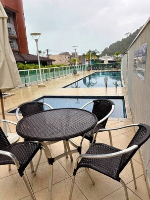 A rooftop pool area with a table and chairs, a view of the pool, and a building in the background.