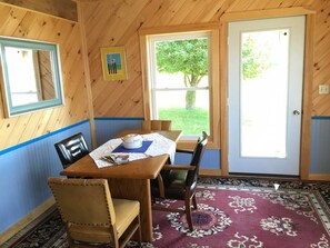 A wooden interior with a dining table, chairs, a rug, and a door leading outside.