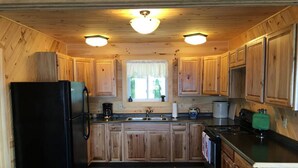 A compact kitchen with wooden cabinets, a black refrigerator, a coffee maker, and a stove. - Sitting on the edge of Cobscook Bay at Rossport by the Sea (Bali)