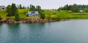 Ein charmantes Cottage mit Dachboden und Blick auf einen stillen See, umgeben von üppiger Vegetation und einigen Häusern.