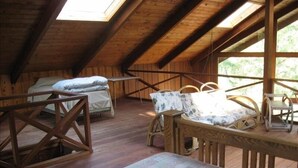A rustic wooden cabin with a loft bedroom, a dining area with a table and chairs, and a large window providing natural light.