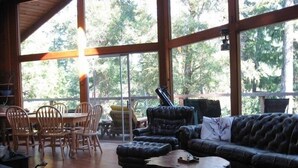 A spacious room with large windows, a wooden dining table with chairs, a leather sofa, and a coffee table.