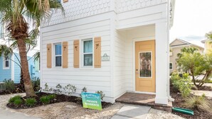 A white building with a yellow door, a sign indicating private residence, and a palm tree in the front yard.