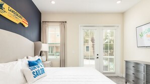 A bedroom with a bed, a nightstand, a lamp, a dresser, and a door with blinds.