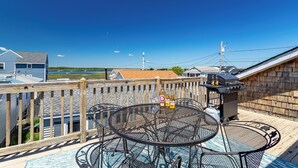 A rooftop patio with a round metal table, a barbecue grill, and a view of a lake and distant buildings.