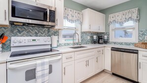 A kitchen with white cabinets, a microwave, a stove, a dishwasher, and a window with patterned curtains.