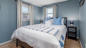 A bedroom with a large bed, two bedside tables with lamps, and a window with curtains.