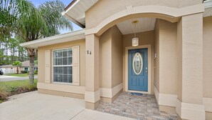 A beige house with a blue door, a number '84' on the wall, and a small porch area. - Heated Pool - 4BR - Sleeps 10 - Pet Friendly (Palm Coast)