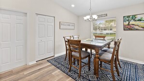 A dining area with a wooden table and chairs, a chandelier, and a welcome sign. - Heated Pool - 4BR - Sleeps 10 - Pet Friendly (Palm Coast)