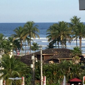 Vista de la playa con palmeras, un edificio de techo de tejas y el océano al fondo.