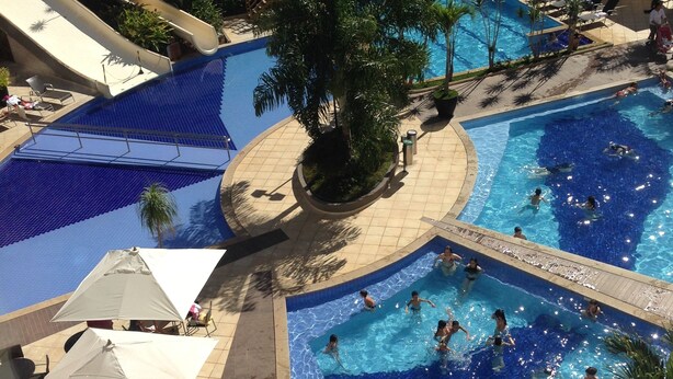 A multi-level pool area with various water features, including slides and a central pool with people swimming. - Luxurious apartment with a 5-star style water park near HOT PARK. (Rio Quente)