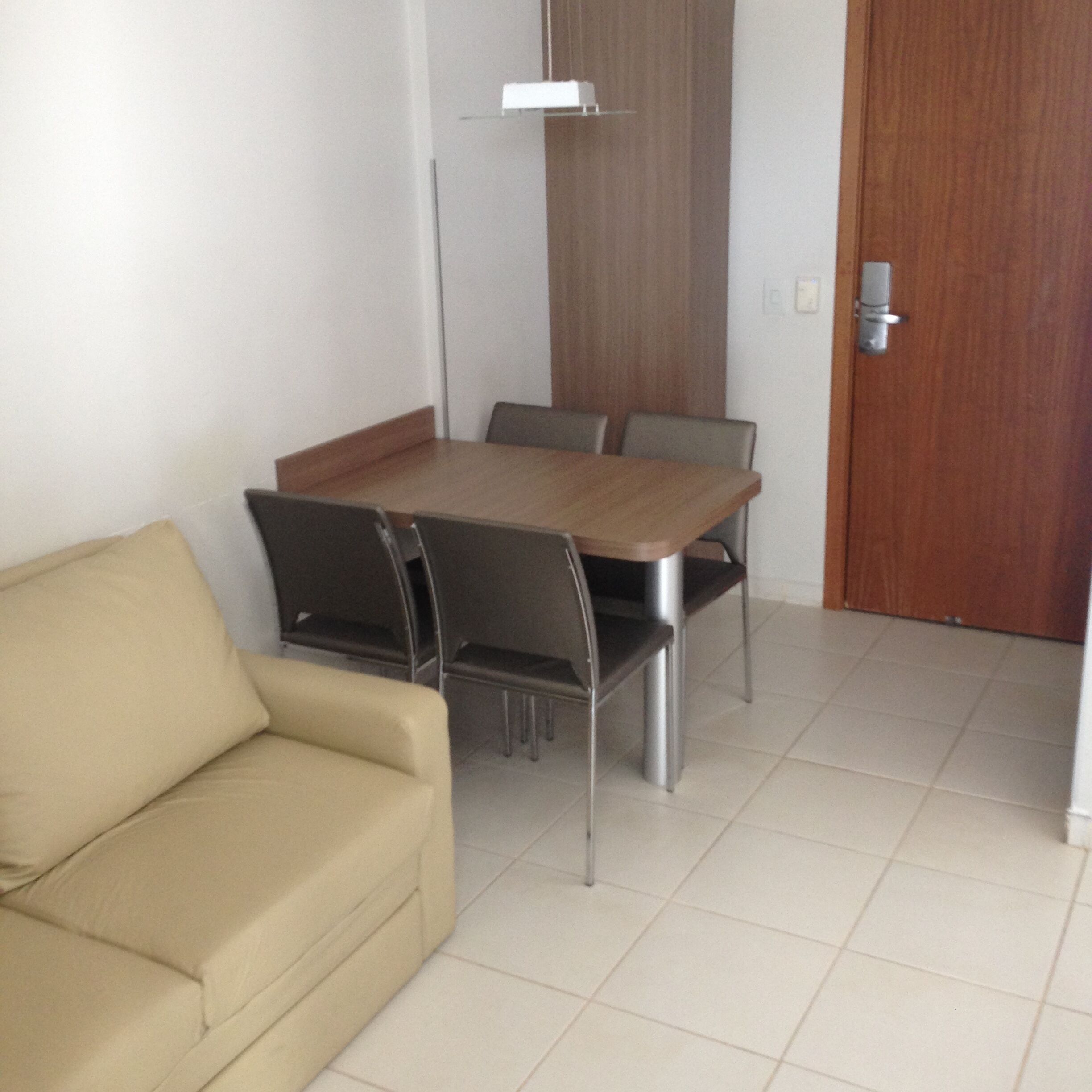 A small room with a wooden dining table, four chairs, a beige sofa, and a wooden door.
