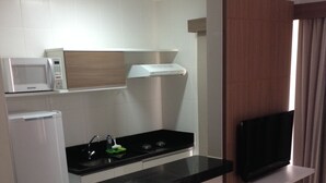 A compact kitchen with a microwave, refrigerator, and stove. There are two black bar stools and a flat-screen TV mounted on the wall. - Luxurious apartment with a 5-star style water park near HOT PARK. (Rio Quente)
