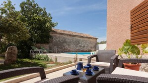 Un espace extérieur aménagé avec des meubles en osier, une table avec des tasses bleues et une vue sur une piscine.