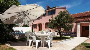 Une terrasse avec une table et des chaises, une piscine et un bâtiment doté d’un toit en tuiles.