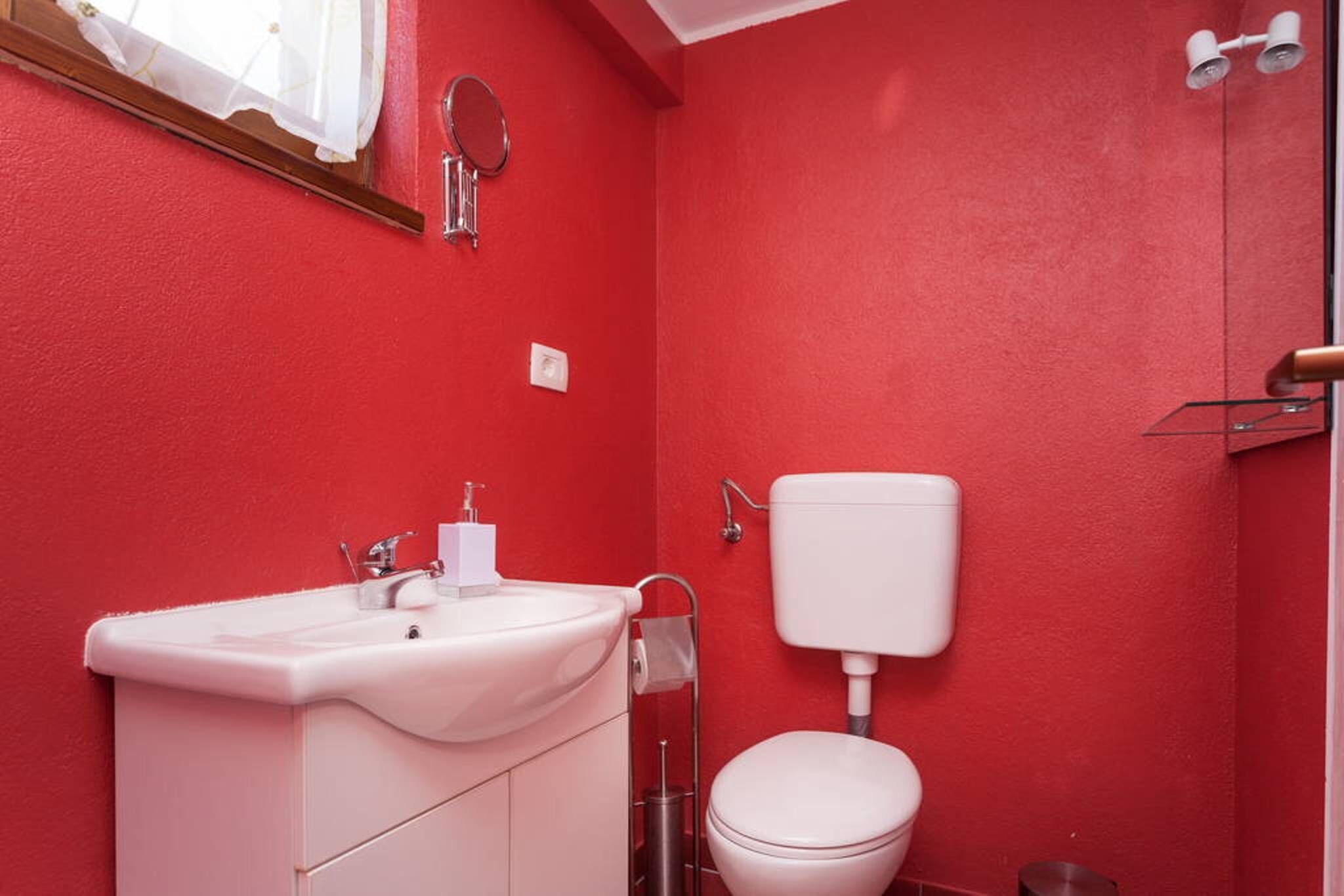 Ein Badezimmer mit roter Wand, weißem Waschbecken und Toilette.